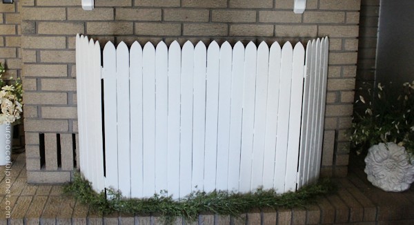 Add some whimsy to your home with this easy DIY picket fence fireplace cover. Made with wood slats and some hinges you can decorate it for any season. 